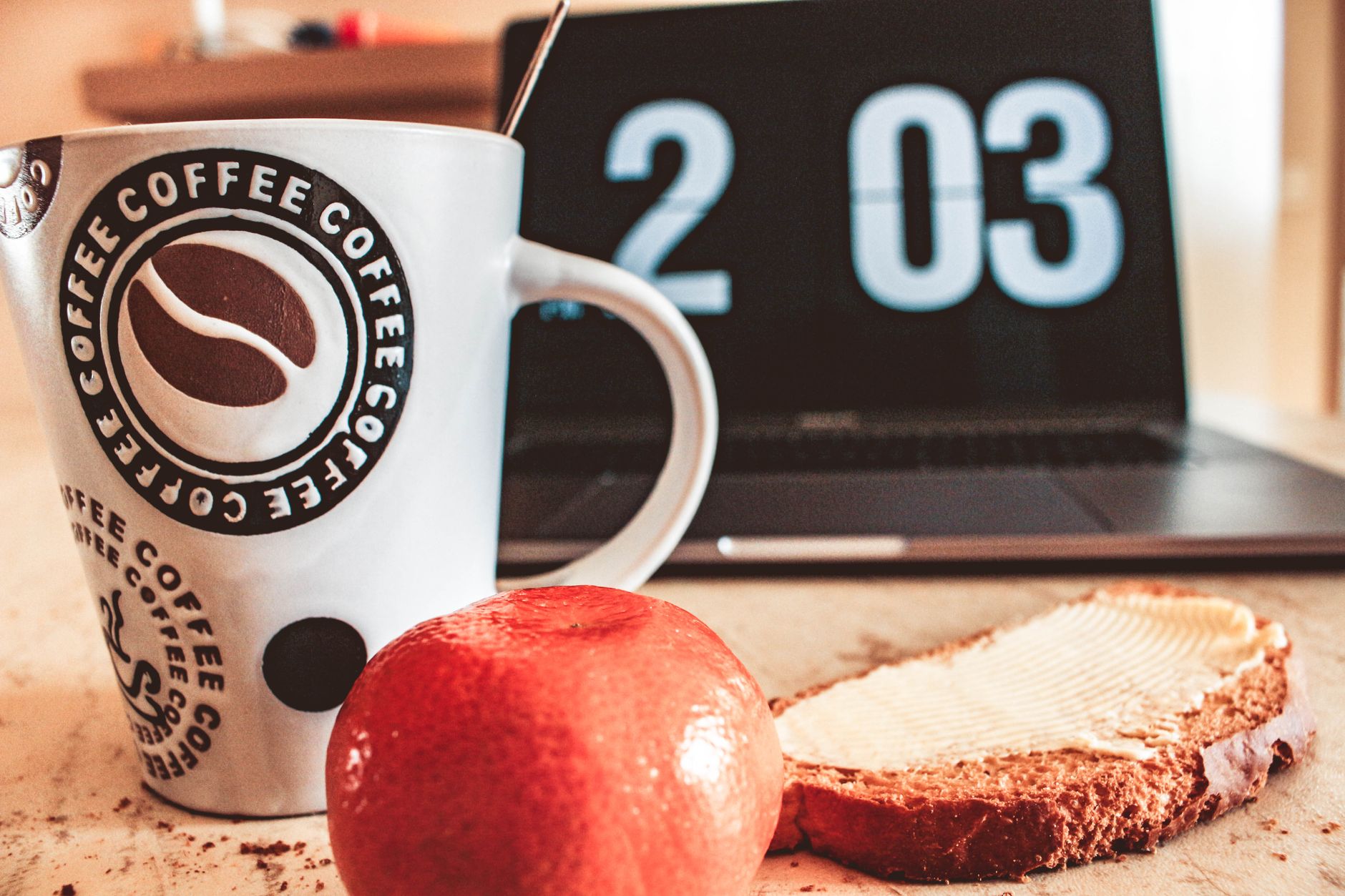 Petit-déjeuner avec café, pain et fruits à côté d'un ordinateur portable, décor de travail depuis chez soi.