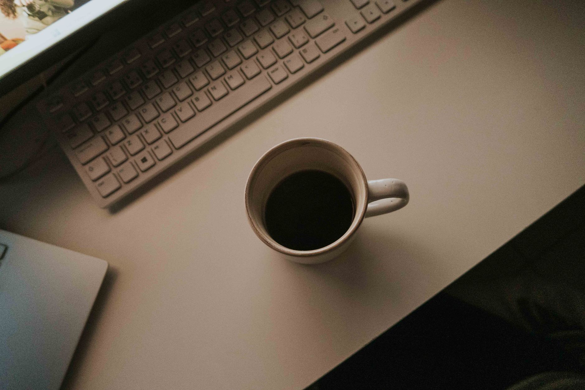 Bureau aux tons chaleureux avec une tasse de café, un clavier et un ordinateur portable.
