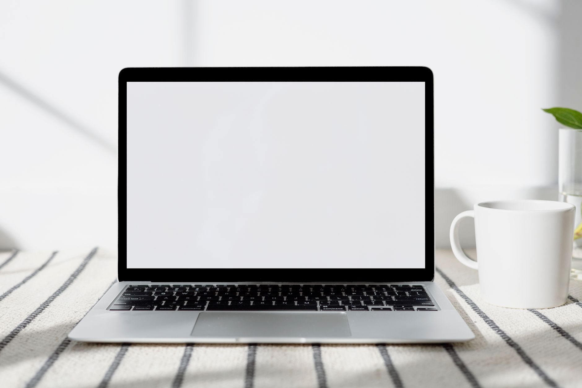 Bureau minimaliste avec un ordinateur portable à écran noir et une tasse, baigné de lumière naturelle.