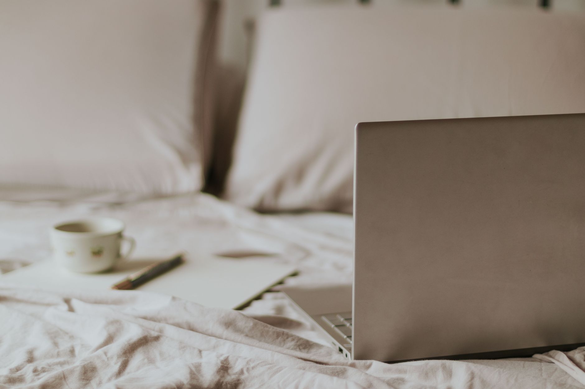 Espace de travail détendu depuis chez soi : ordinateur portable, tasse de café et bloc-notes sur un lit.